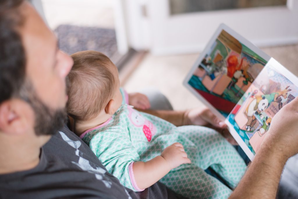 Man is reading for an infant resting on his chest from a picture book