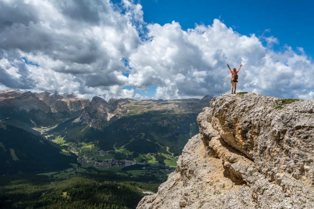 Woman standing on top of a cliff overlooking a green valley